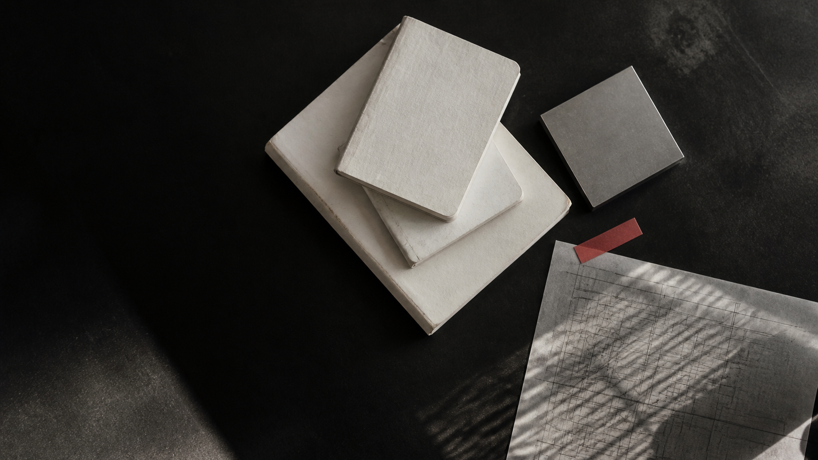 Research notebooks and a drafting sheet on a dark worktable